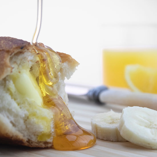 runny honey being drizzled over french stick with sliced banana