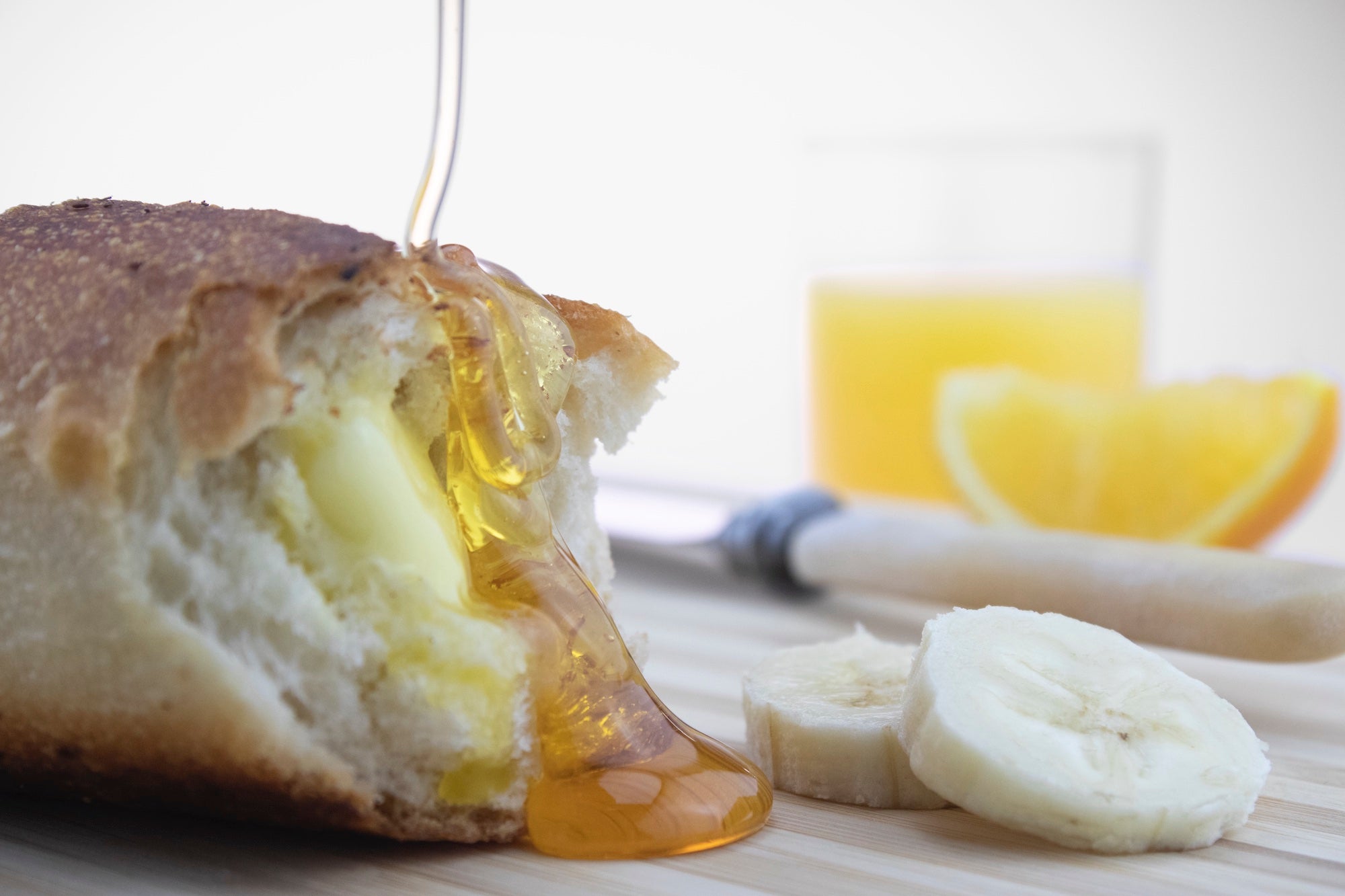 runny honey being drizzled over french stick with sliced banana